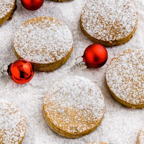 round polvorones cookies on parchment paper with red Christmas bulbs around.