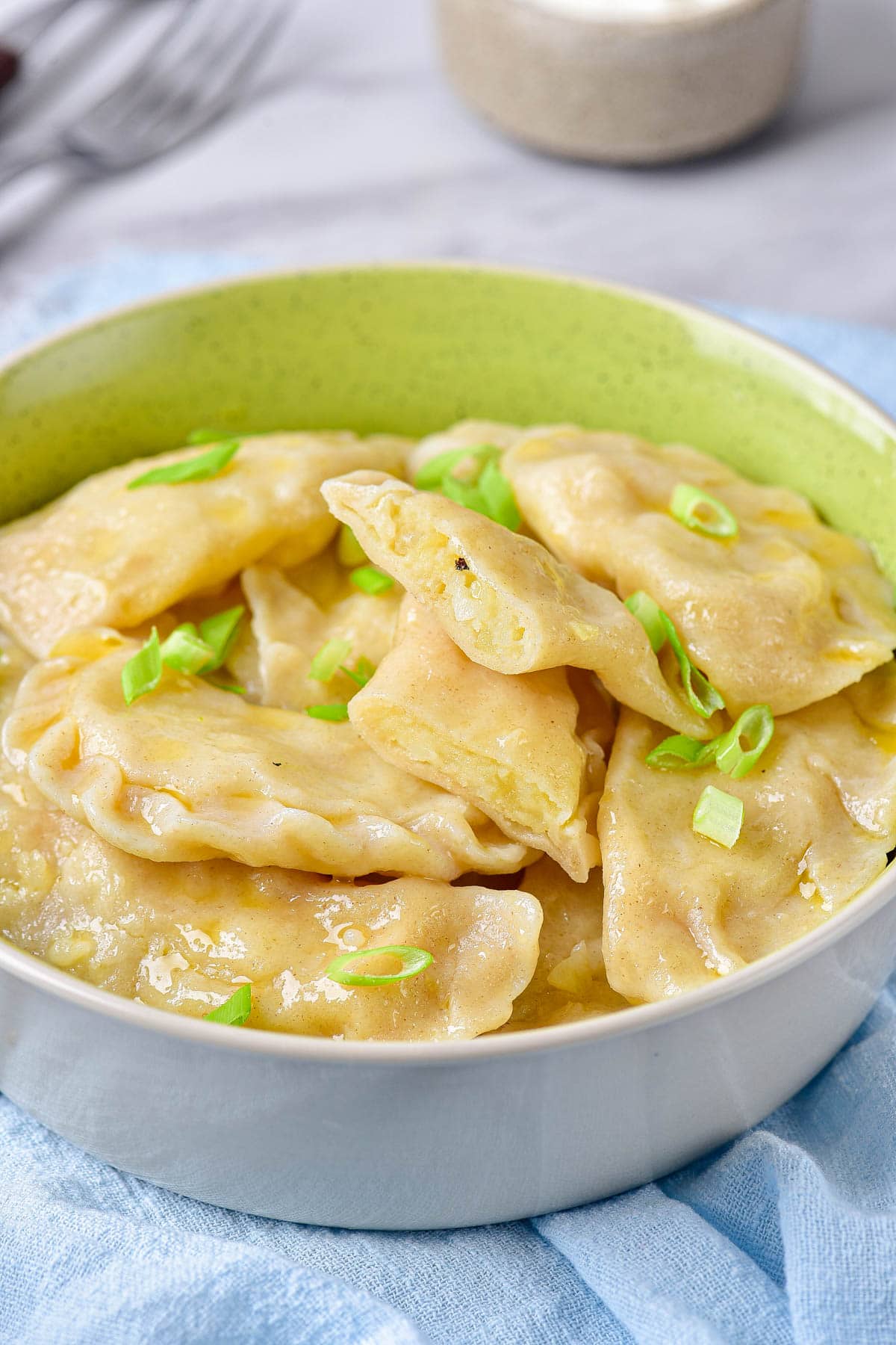 boiled varenyky dumplings in bowl with sliced green onion on top with one cut open to reveal potato filling.