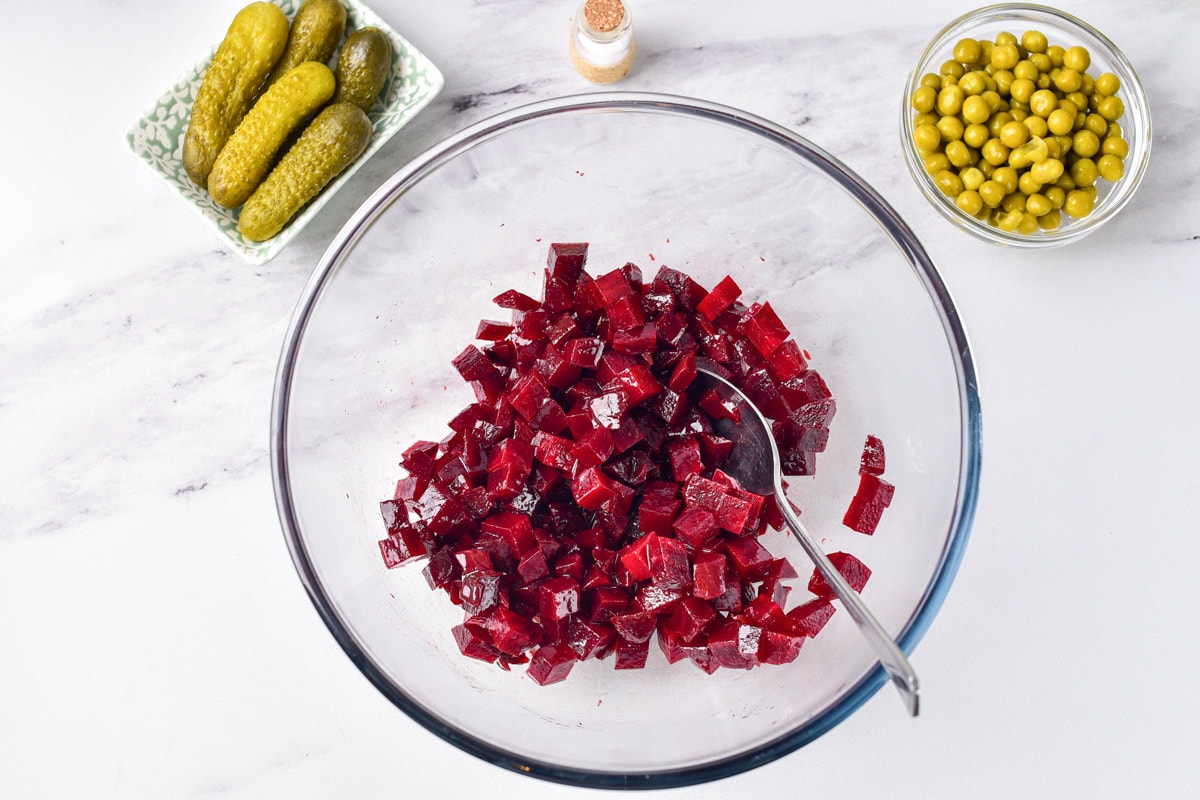 chopped beets in clear glass bowl on counter top with chopped ingredients in bowls beside.