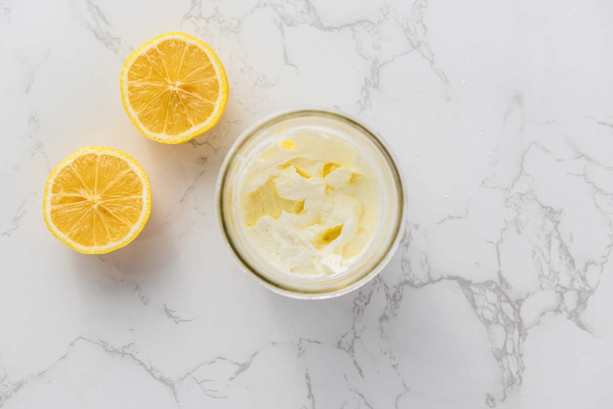 whipped cream in glass with cut lemon beside on counter.