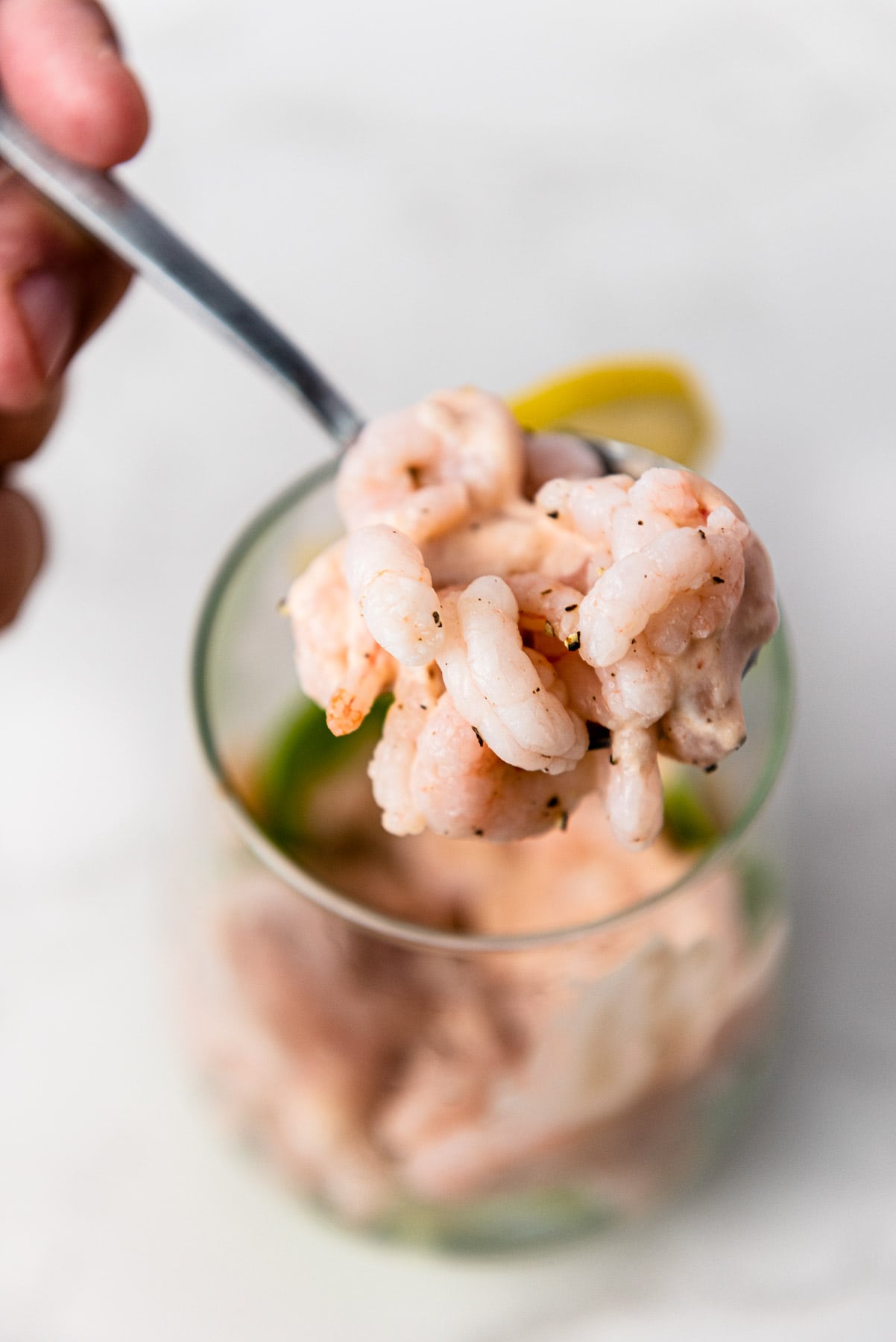 hand holding spoon lifting cooked shrimp and dressing out of serving glass.