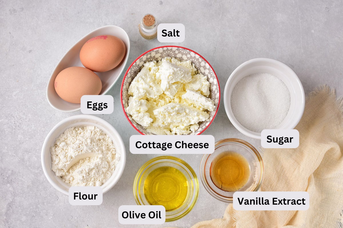 ingredients to make cottage cheese pancakes in bowls on grey counter top with labels.