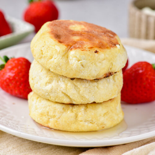 stack of three cottage cheese pancakes on white plate with strawberries around.
