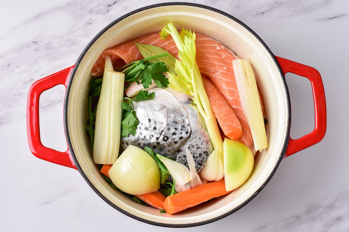 raw salmon in red handled pot with other vegetables sitting on grey counter.