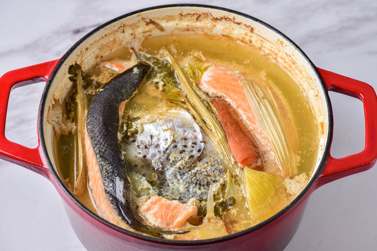 boiled fish soup in red pot on grey counter top.