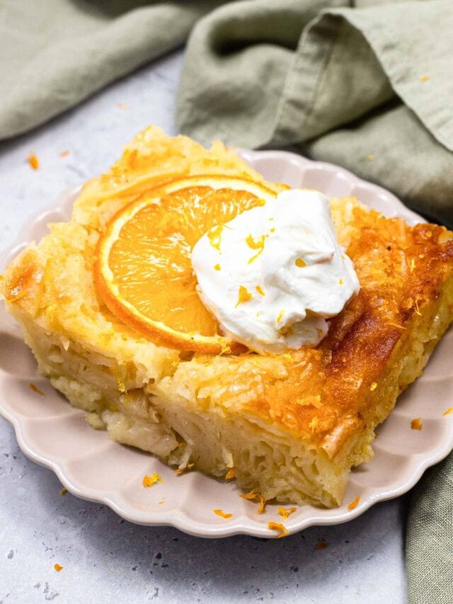 piece of greek orange syrup cake with orange slice and whipped cream on top sitting on plate.