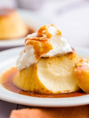 Flan spanish flan on plate with whipping cream and sauce on top with chunk taken from it.