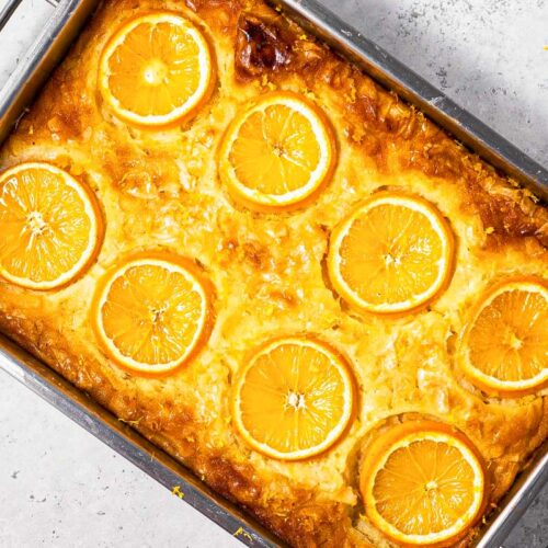 orange syrup cake in pan with sliced oranges on top sitting on grey counter top.