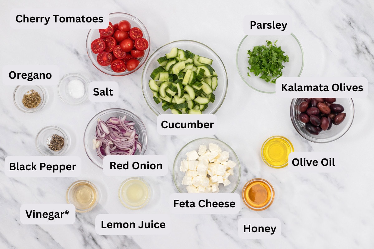 ingredients to make greek salad in bowls on counter with labels.