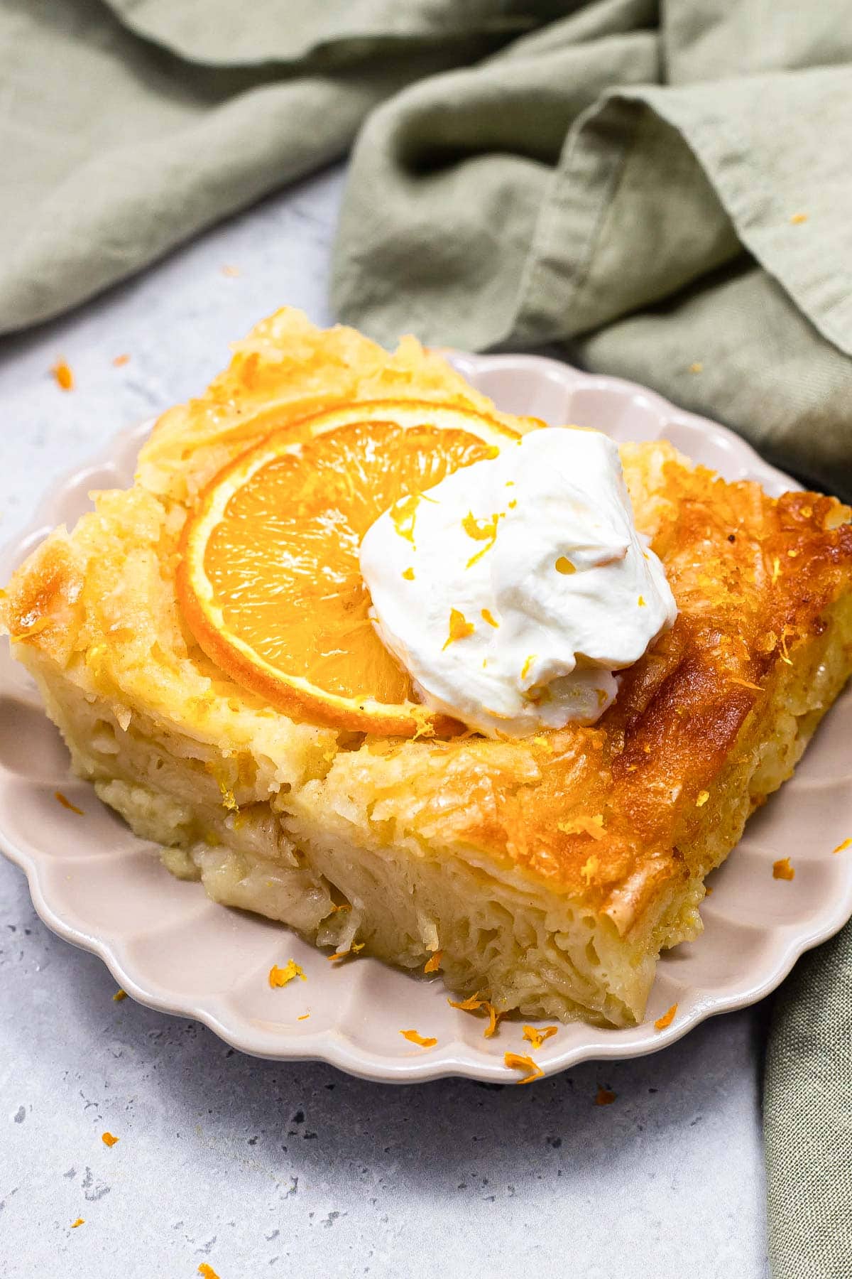 piece of greek orange syrup cake with orange slice and whipped cream on top sitting on plate.