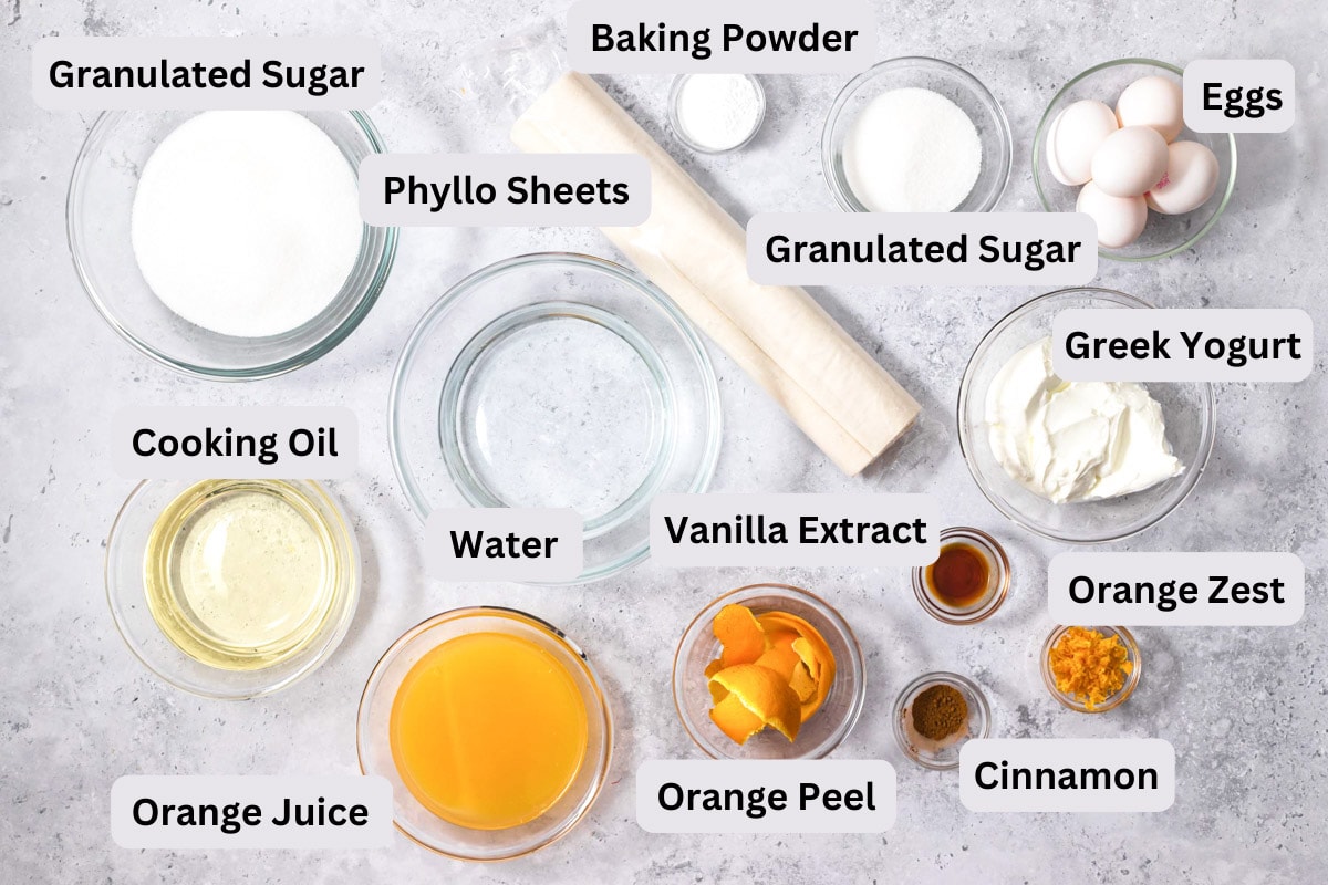 ingredients to make greek orange cake on grey counter with labels.