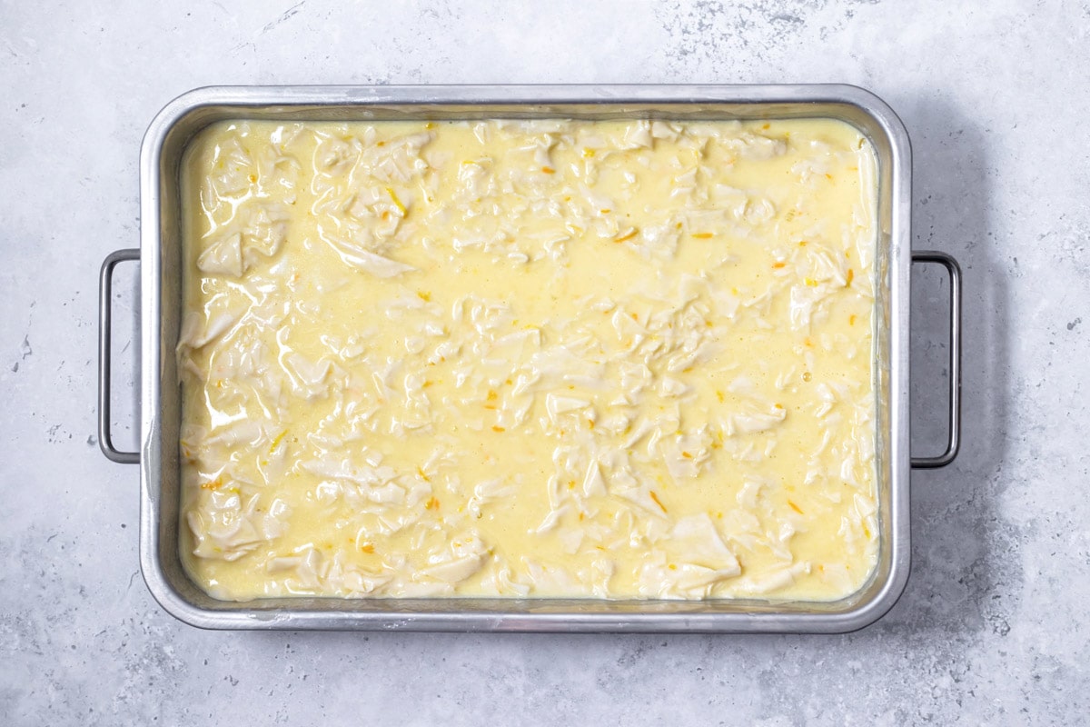 cake pan filled with light yellow liquid and shredded phyllo sheets sitting on grey counter.