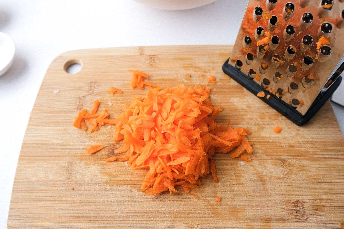 grated orange carrot on wooden cutting board with box grated beside.