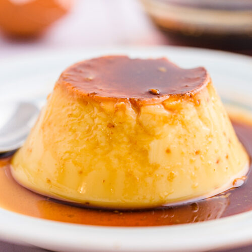 flan covered in sauce on white plate with spoon beside.
