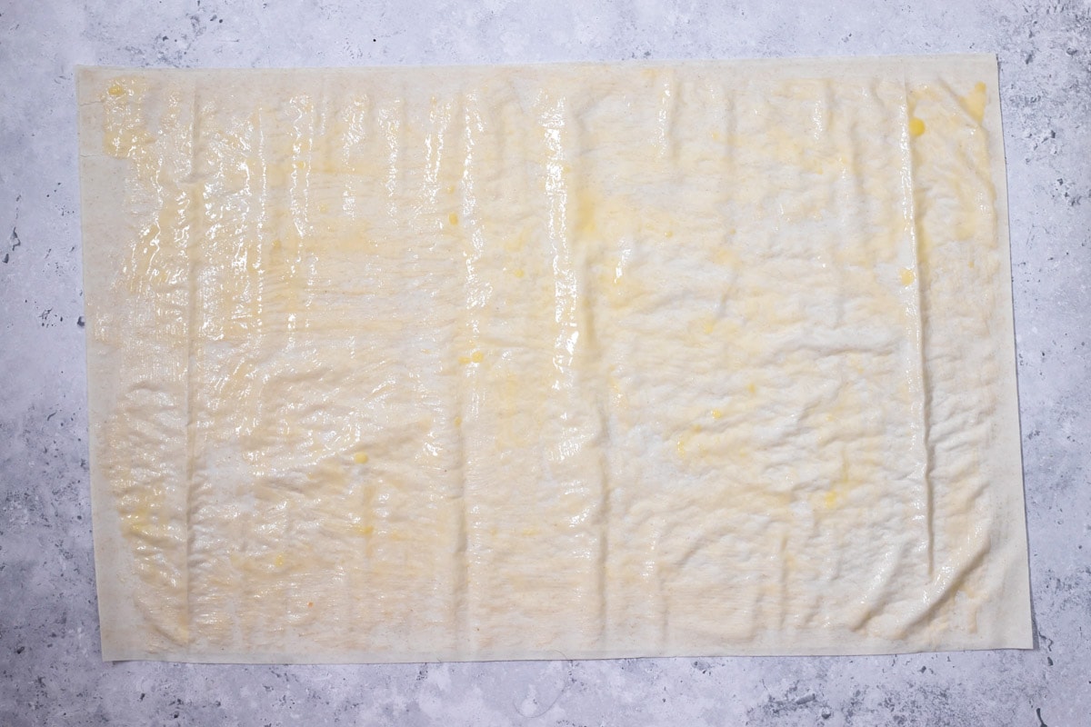 sheet of phyllo dough rolled out on grey counter and covered in butter.