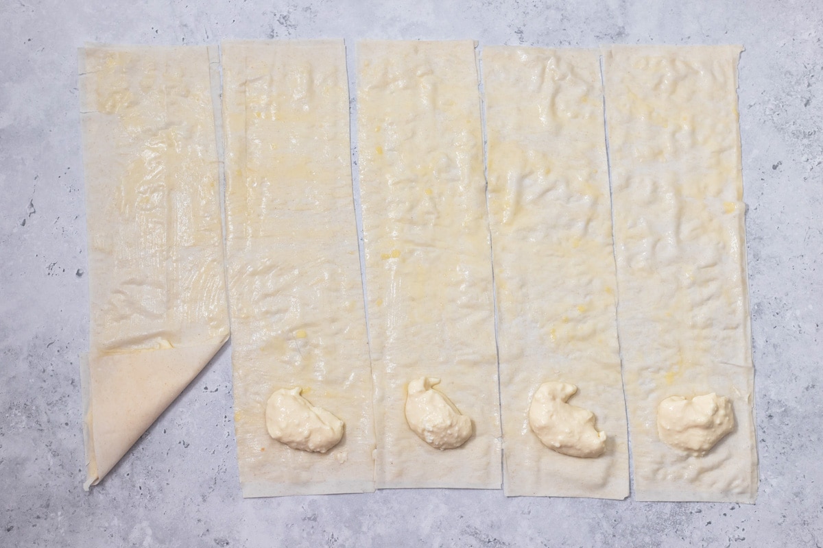 strips of phyllo dough on grey counter with cheese filling at the ends with one folded over.