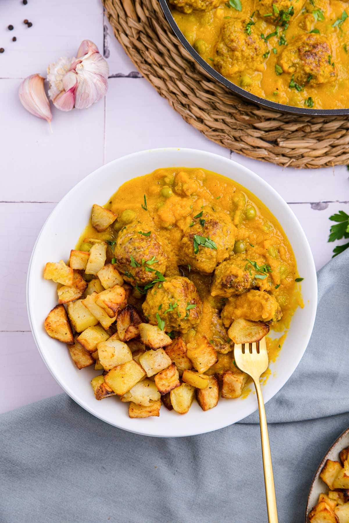 spanish meatballs with potatoes and thick yellow sauce on plate with gold fork sticking out.