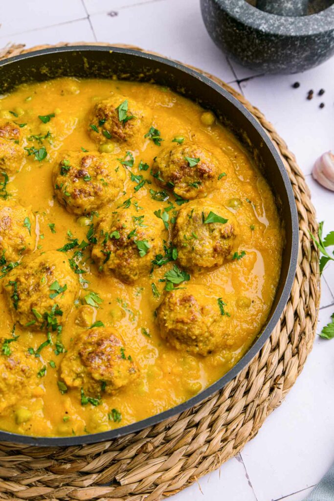 large black sauce pan filled with cooked meatballs sitting in yellow sauce.