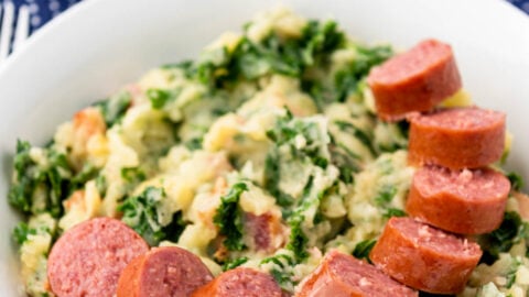 white bowl full of cut up sausage and mashed potatoes with blue cloth behind.