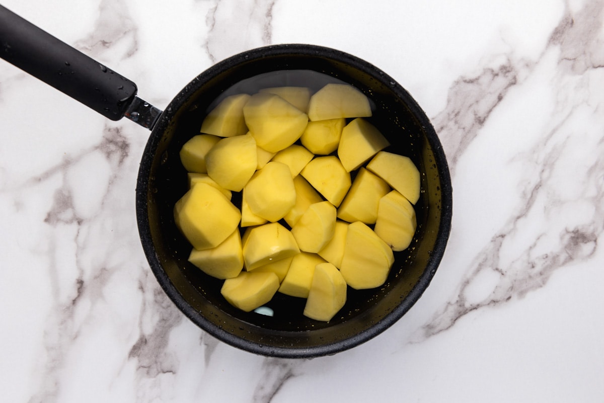 cut up raw potatoes sitting in water in black pot with marble counter around.