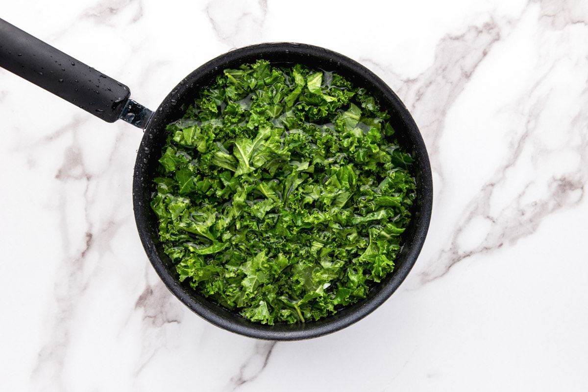 chopped kale sitting in water in black pot with counter top around.