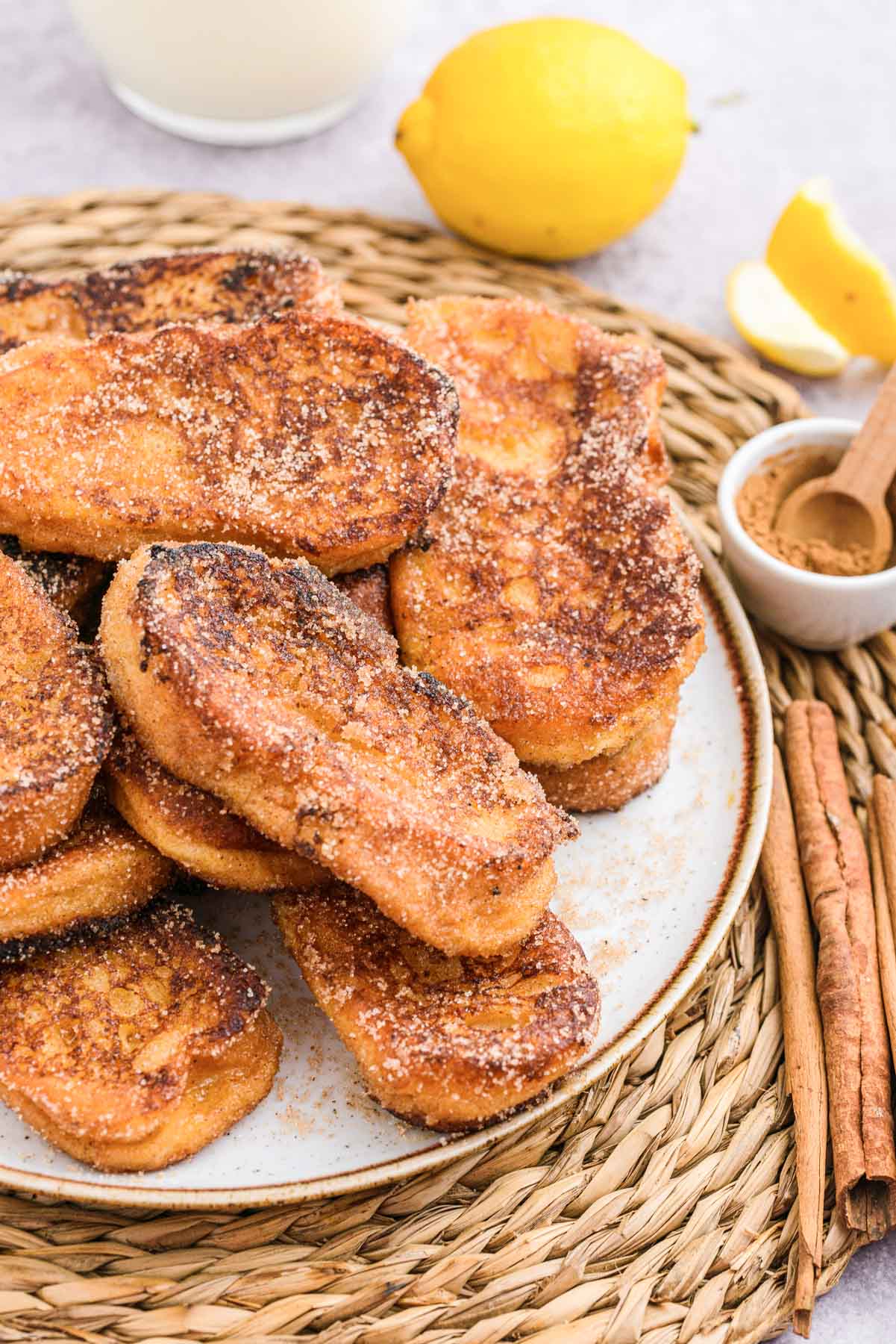 pile of french toast on white plate sitting on wicker placemat with lemon beside.