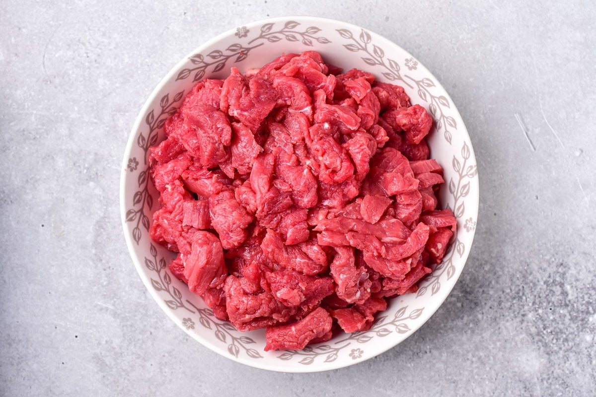 red raw beef chunks in bowl on grey counter.