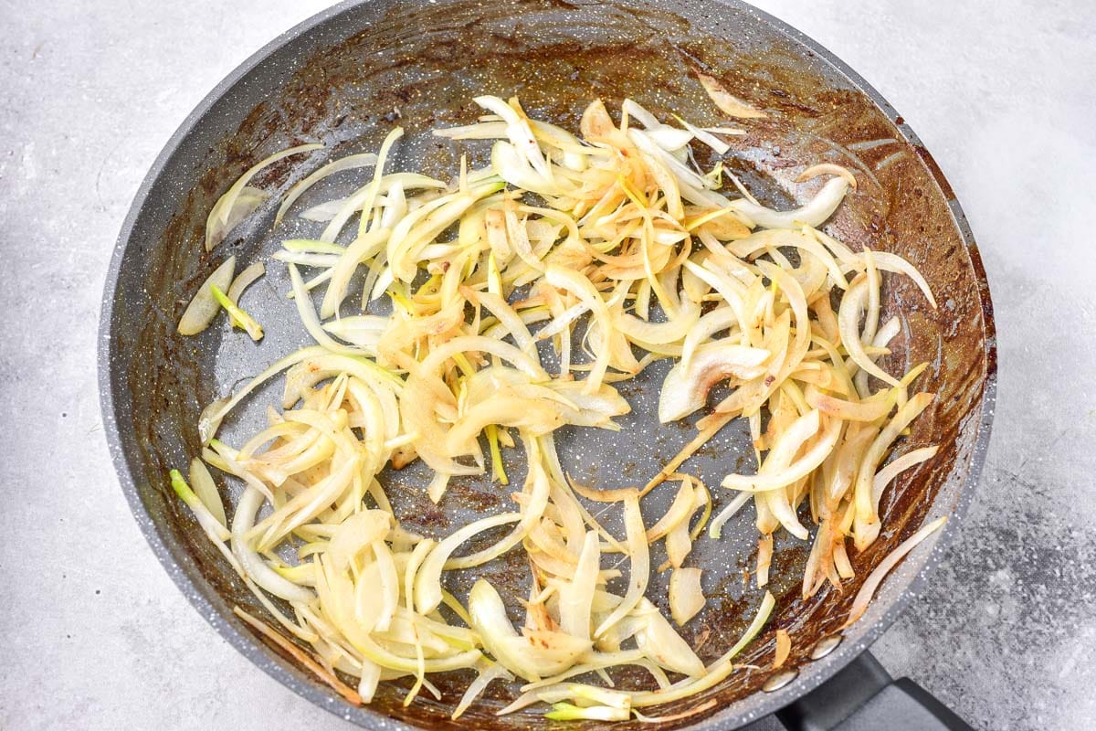 thinly sliced onions browning in frying pan with grey counter around.