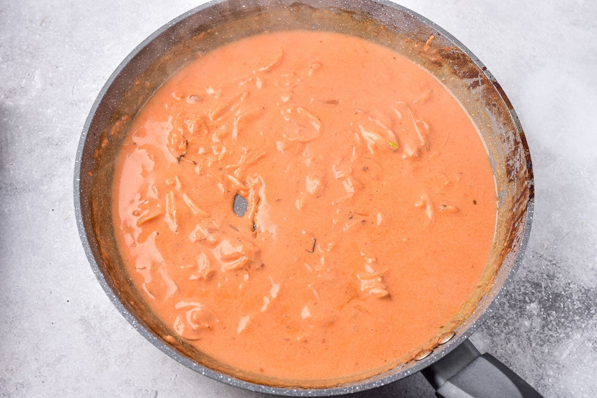 thickened orange sauce in frying pan with grey counter around.