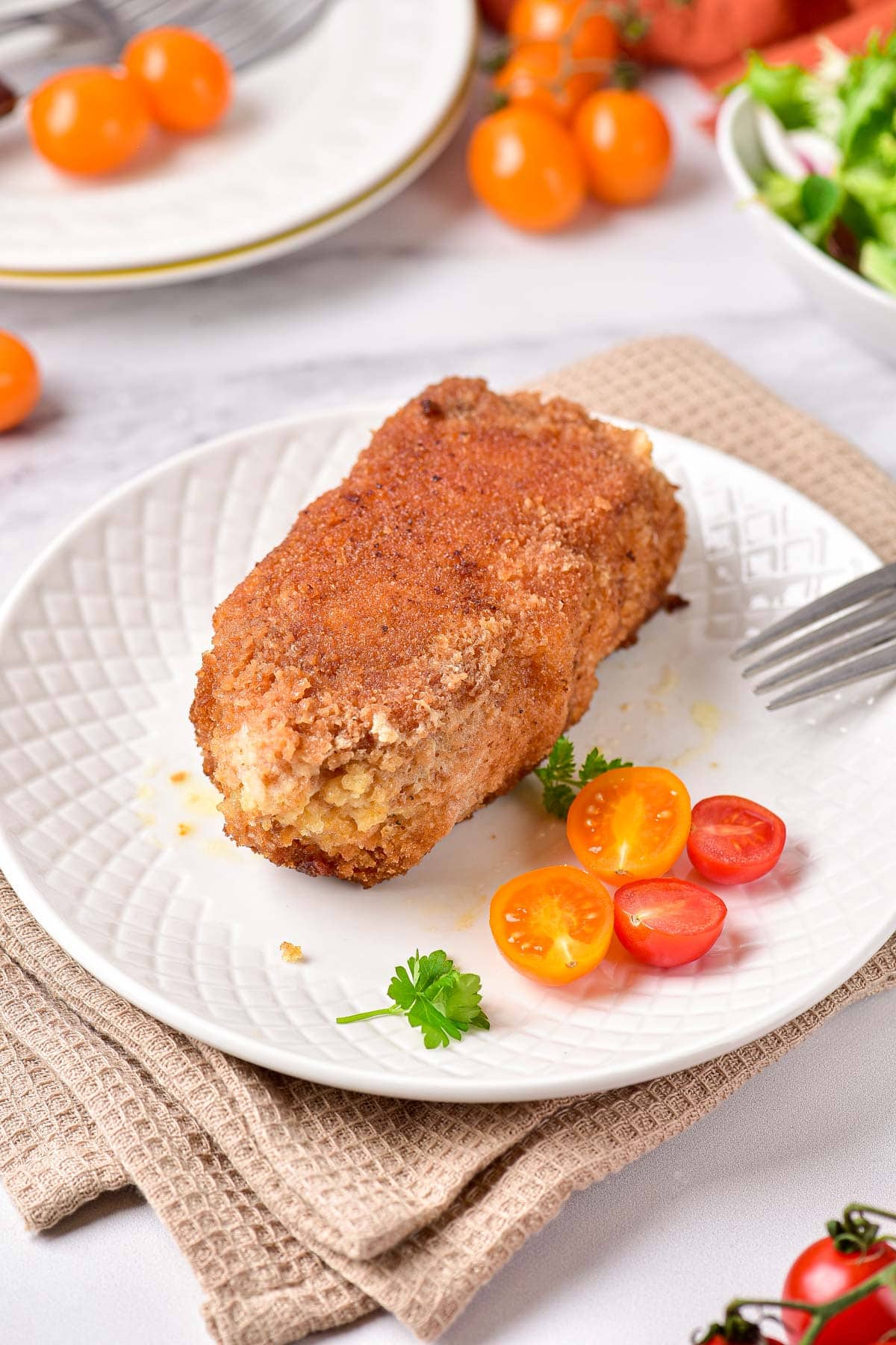 crispy chicken kiev on plate with tomatoes on top and cloth underneath.