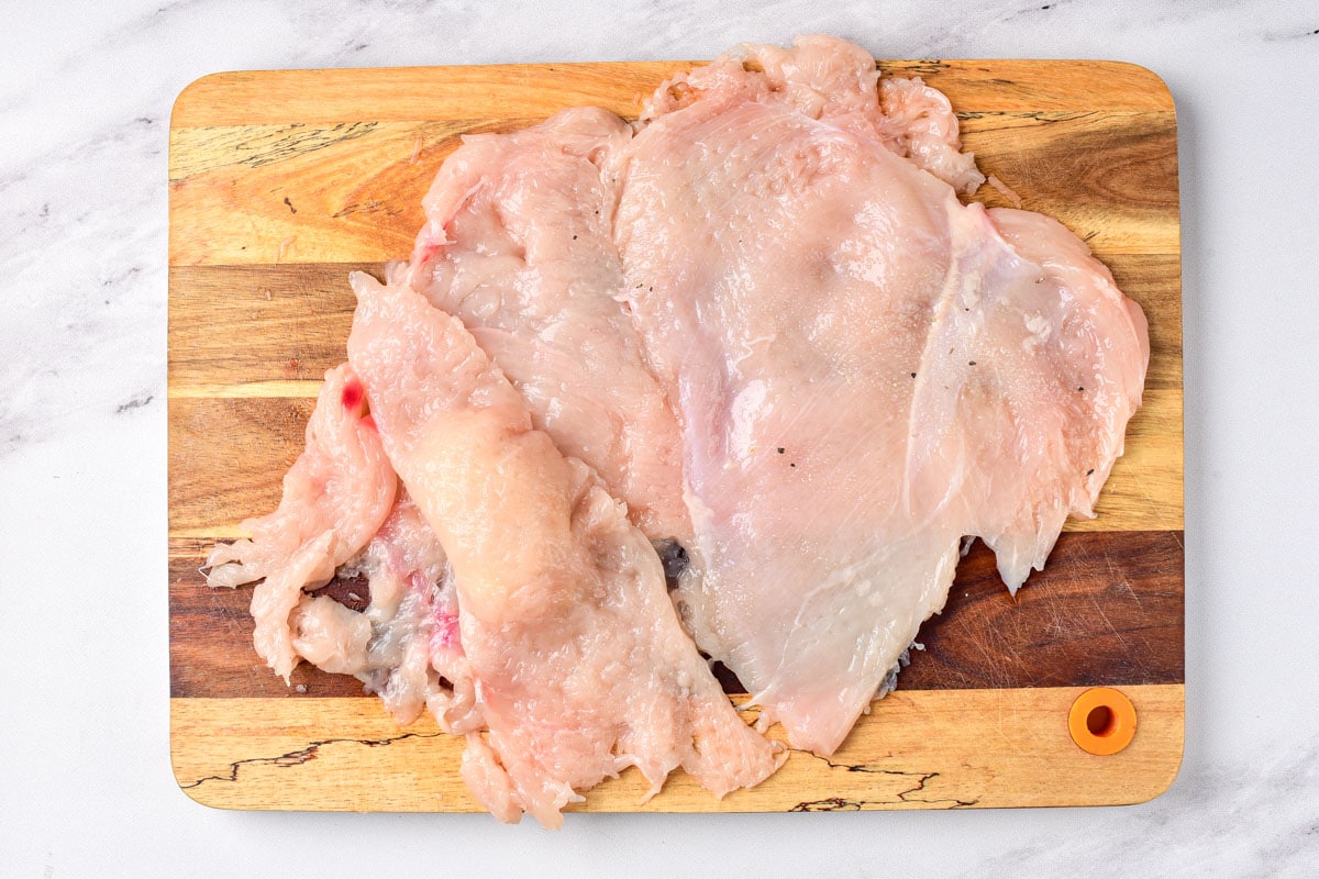 flattened chicken breast on wooden cutting board.