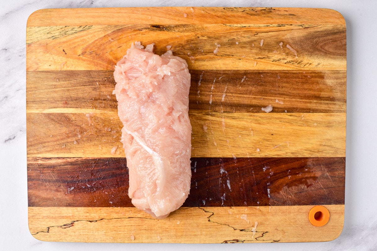 chicken breast wrapped around garlic butter sitting on wooden cutting board.
