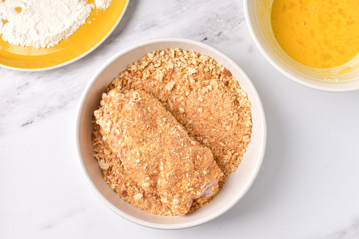 raw chicken breast coated in breadcrumbs sitting on plate on counter top.