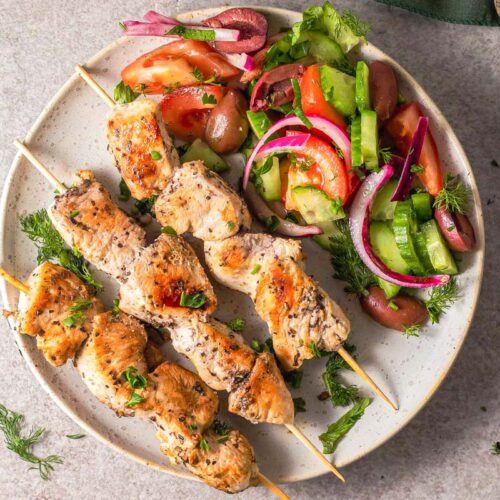 grilled skewers of chicken souvlaki on plate with green cloth beside.
