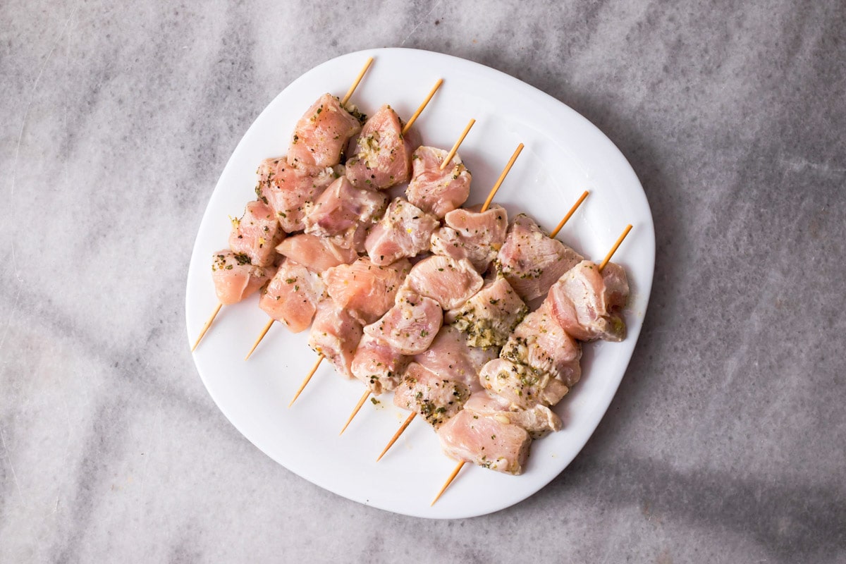 wooden skewers with pieces of marinaded chicken on them sitting on white plate.