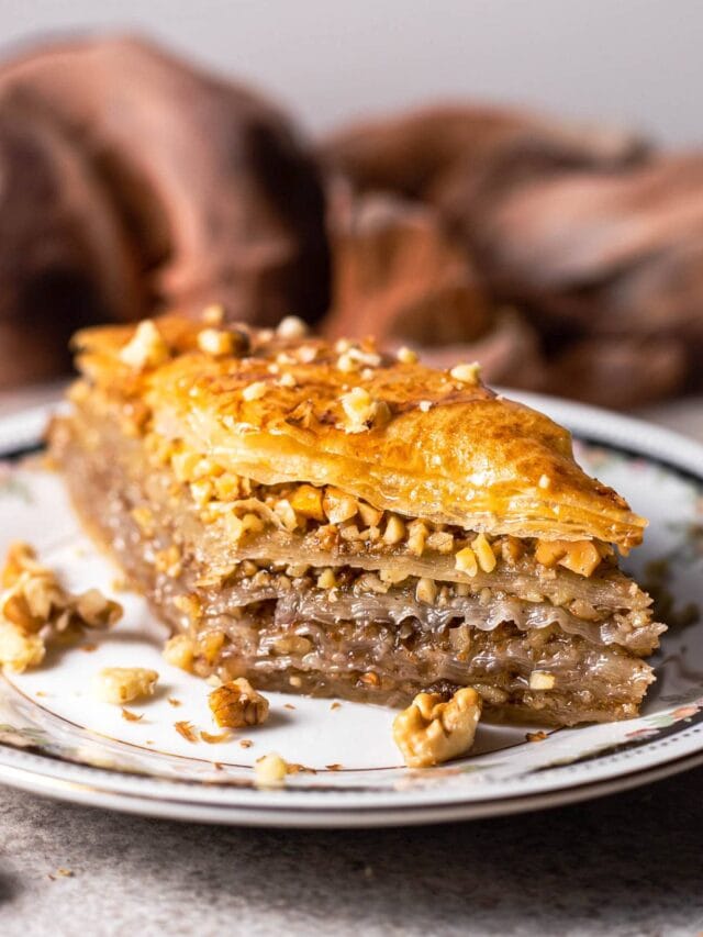 slice of greek baklava with layers and nuts on plate with brown cloth behind.