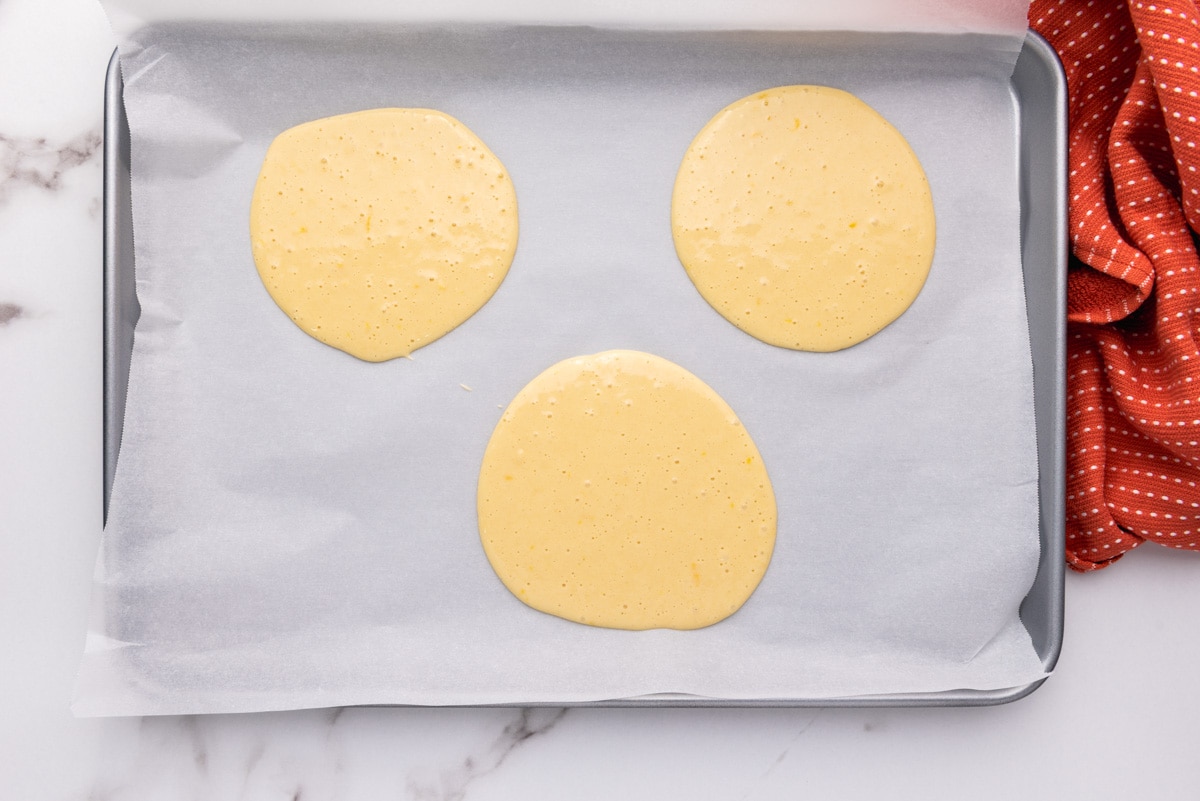 three circles of egg cake batter on parchment paper pan.