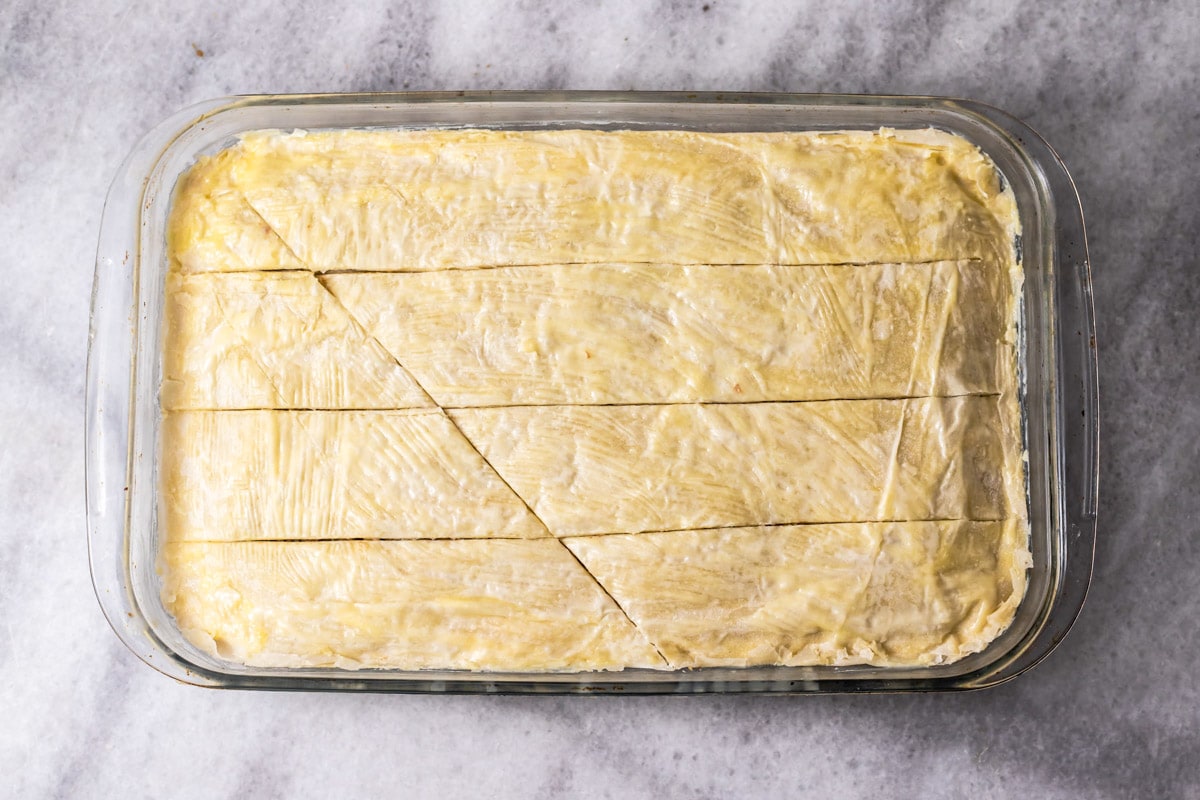 layers of nuts and phyllo dough in glass pan with knife cuts through it.