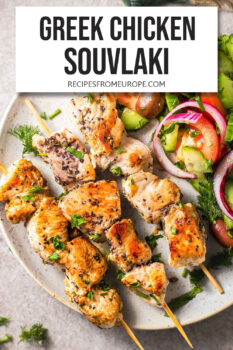 plate with cooked pieces of chicken on skewers and Greek salad plus text overlay "Greek chicken souvlaki".