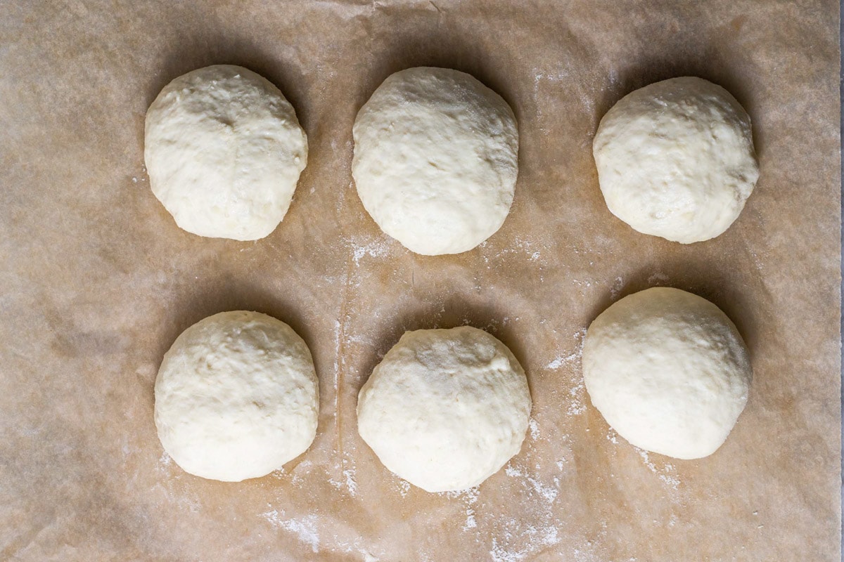 six balls of raw dough sitting on brown parchment paper.
