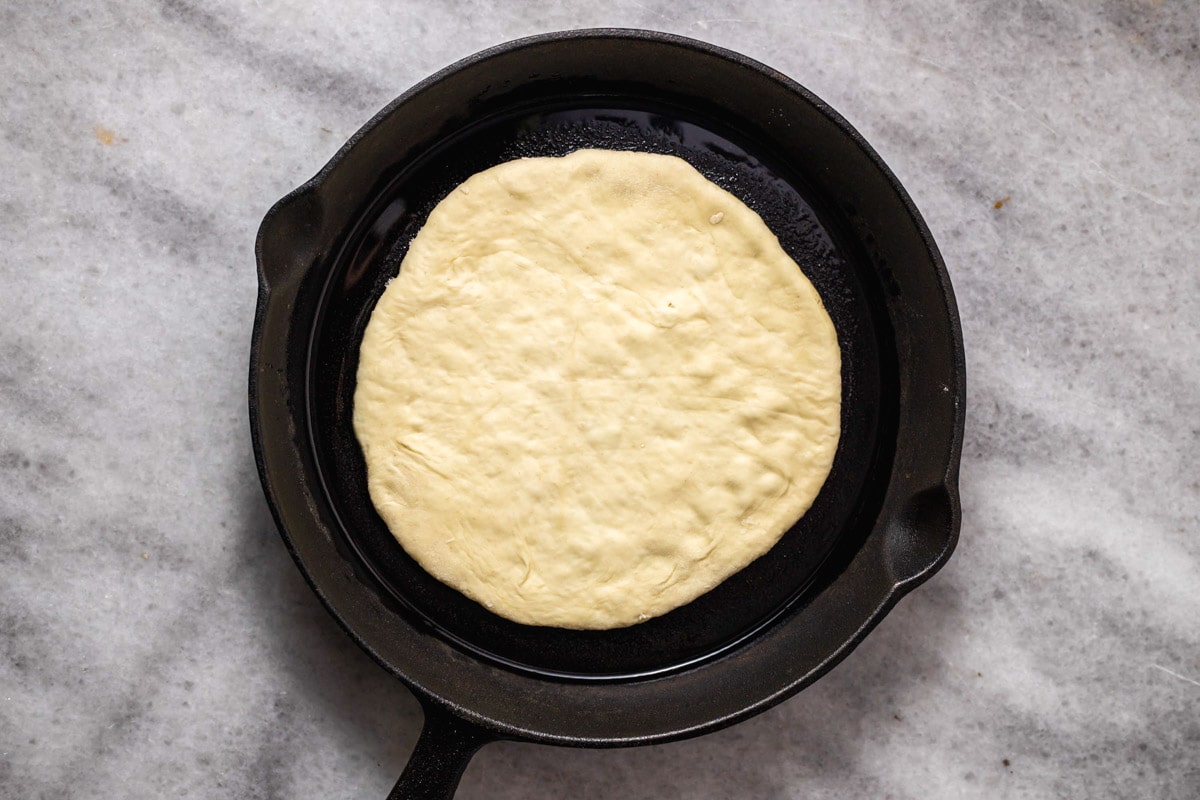 raw circle of pita dough sitting in black cast iron pan.