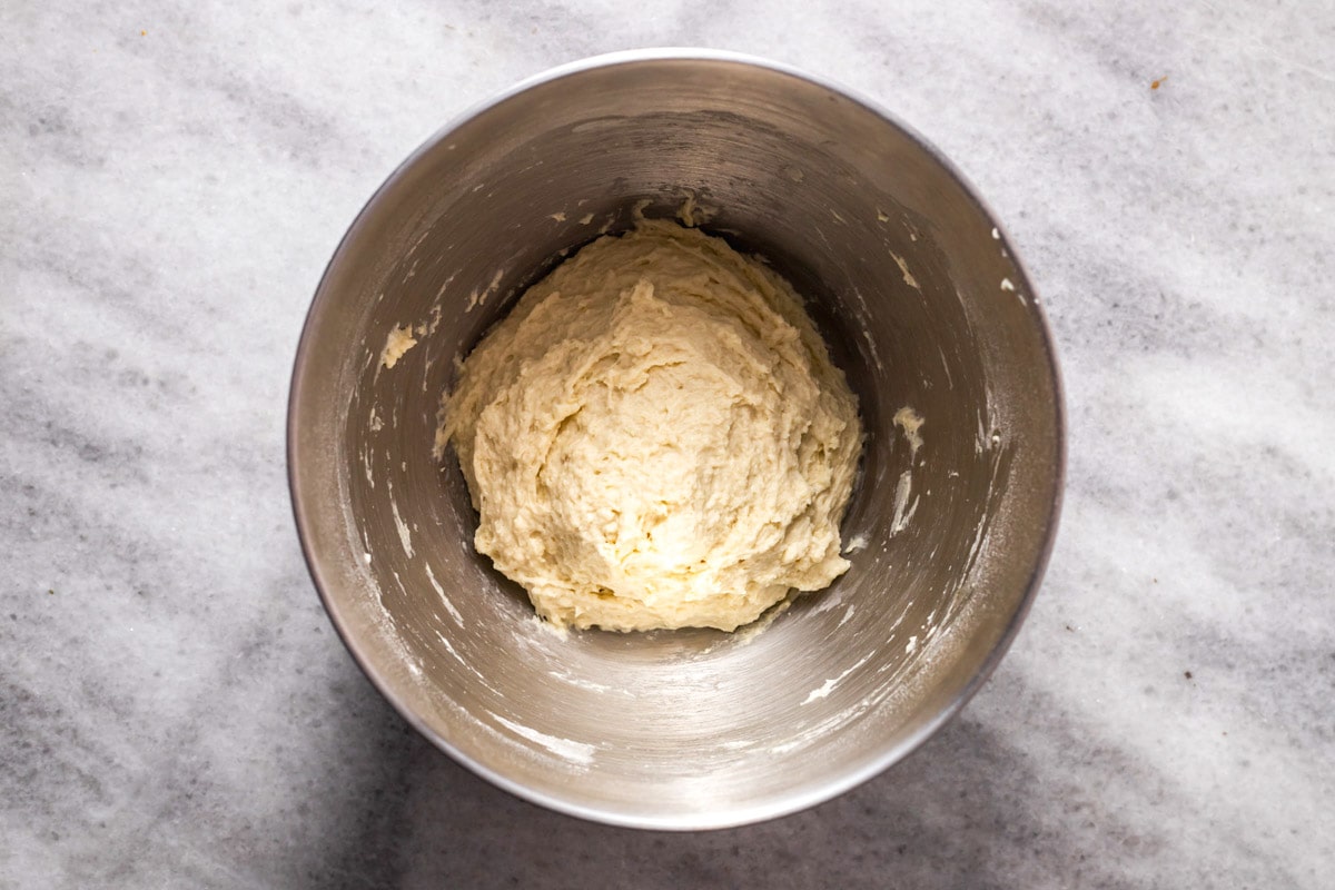 raw dough for pita bread sitting in a ball in silver mixing bowl on counter.