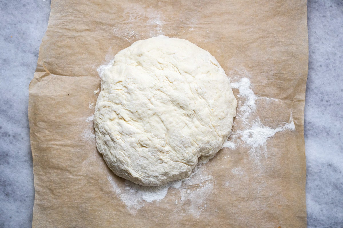 large ball of pita dough on brown parchment paper.