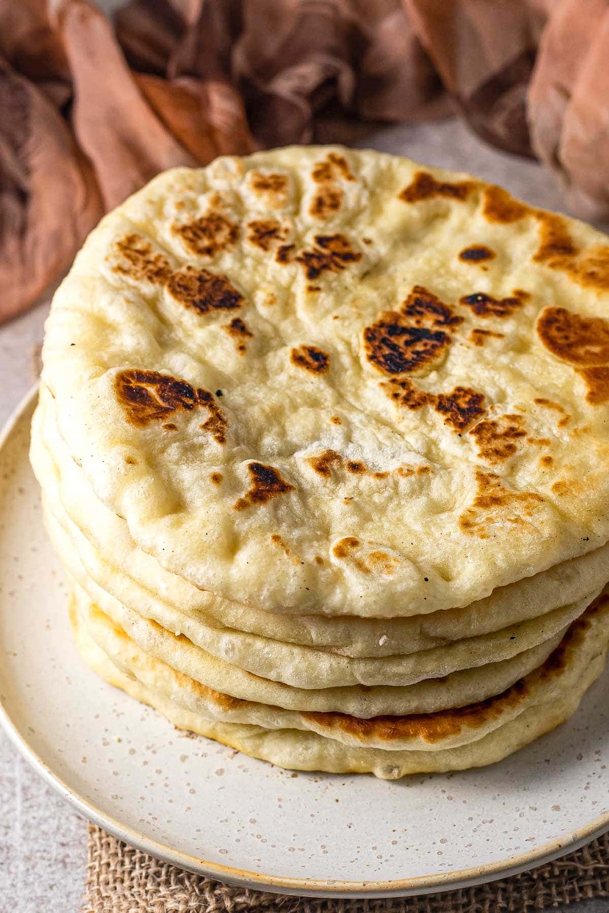 tall stack of pita bread on plate with orange cloth behind.