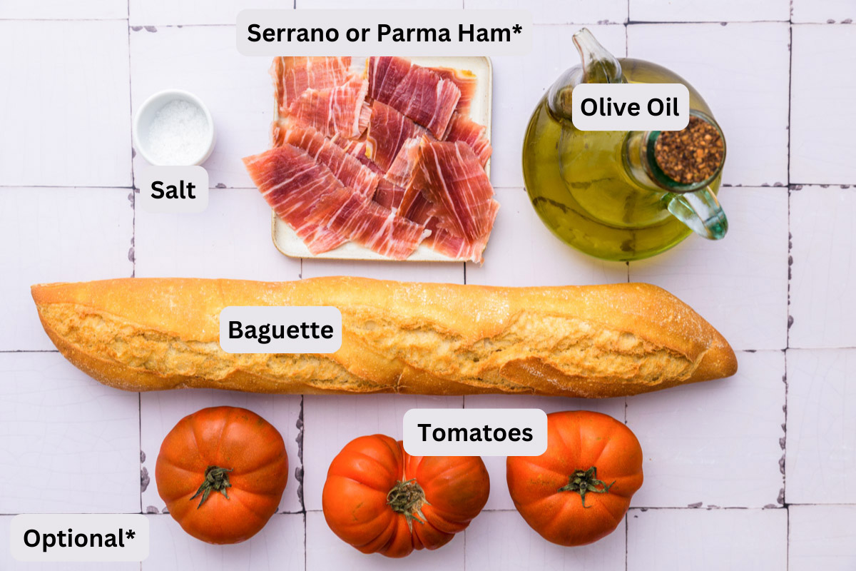 ingredients to make spanish tomato bread on white tiled counter with labels.