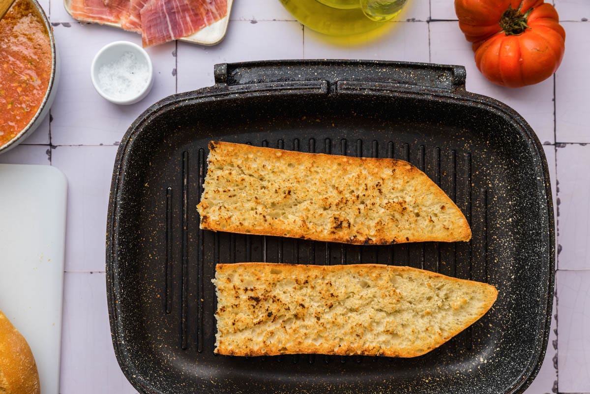 two halves of baguette toasting in black cast iron pan.