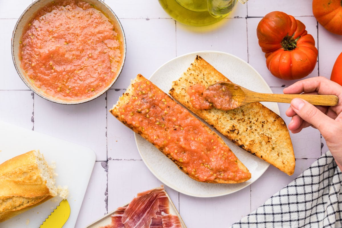 wooden spoon placing tomato mixture on toasted pieces of baguette on white plate.