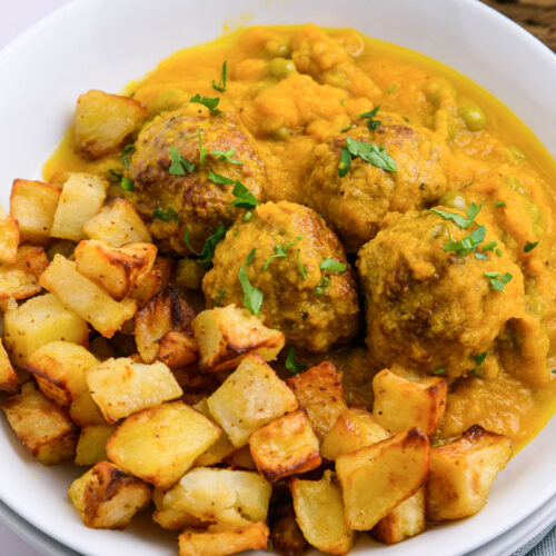 white dish of spanish meatballs and fried potatoes in yellow sauce.