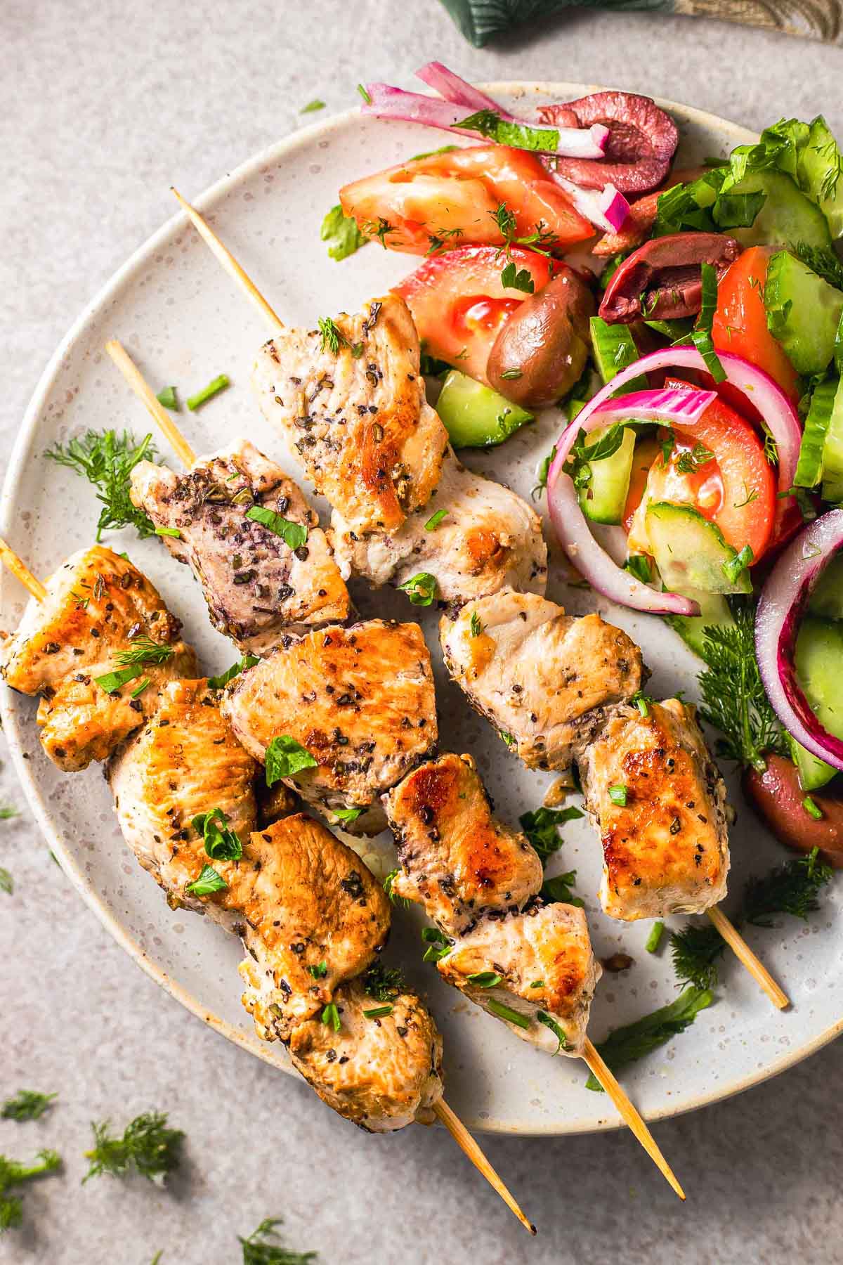 grilled pieces of chicken on wooden skewers on white plate with salad beside.