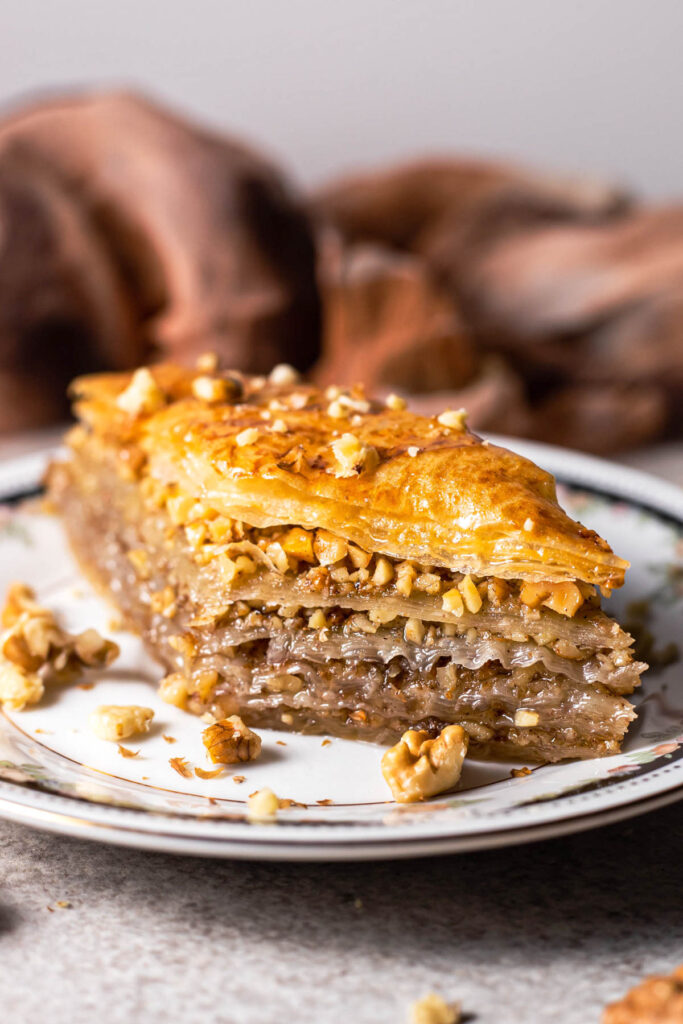slice of greek baklava with layers and nuts on plate with brown cloth behind.